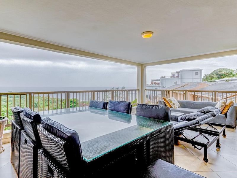A spacious covered balcony featuring tiled flooring, a protective metal balustrade, and expansive views of the surrounding landscape and ocean.