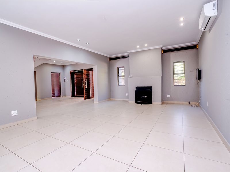 Spacious, light-filled living room featuring neutral tiled flooring, a built-in fireplace, recessed lighting, and a wall-mounted air conditioning unit.