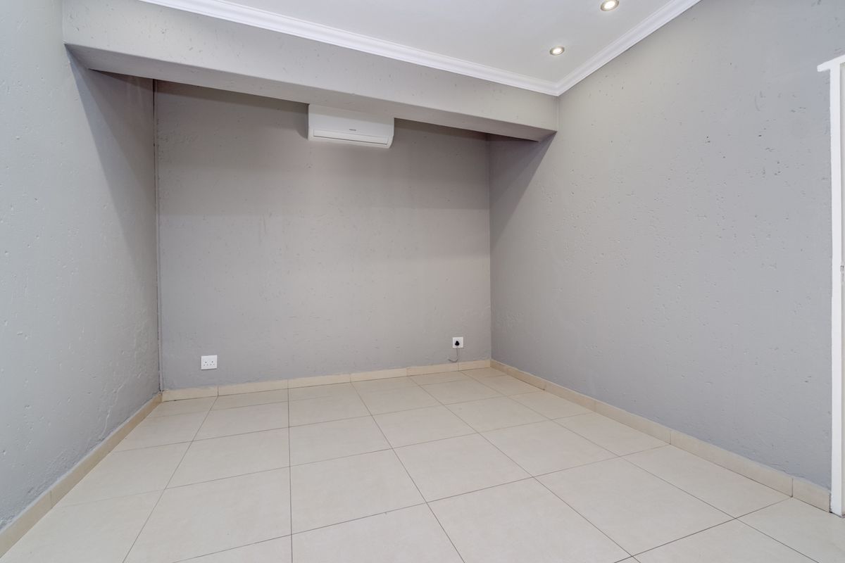 A clean, empty bedroom featuring neutral grey walls, tiled flooring, recessed lighting, and a wall-mounted air conditioning unit.