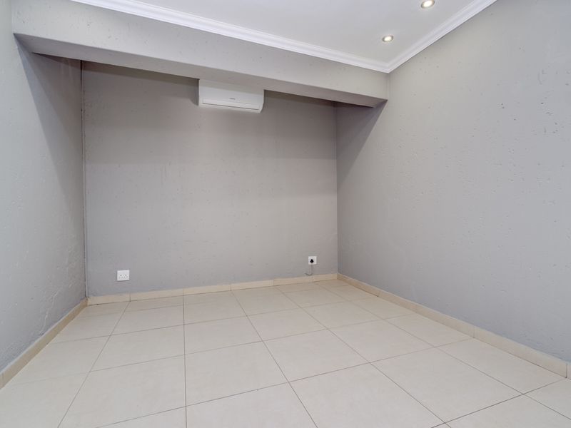 A clean, empty bedroom featuring neutral grey walls, tiled flooring, recessed lighting, and a wall-mounted air conditioning unit.