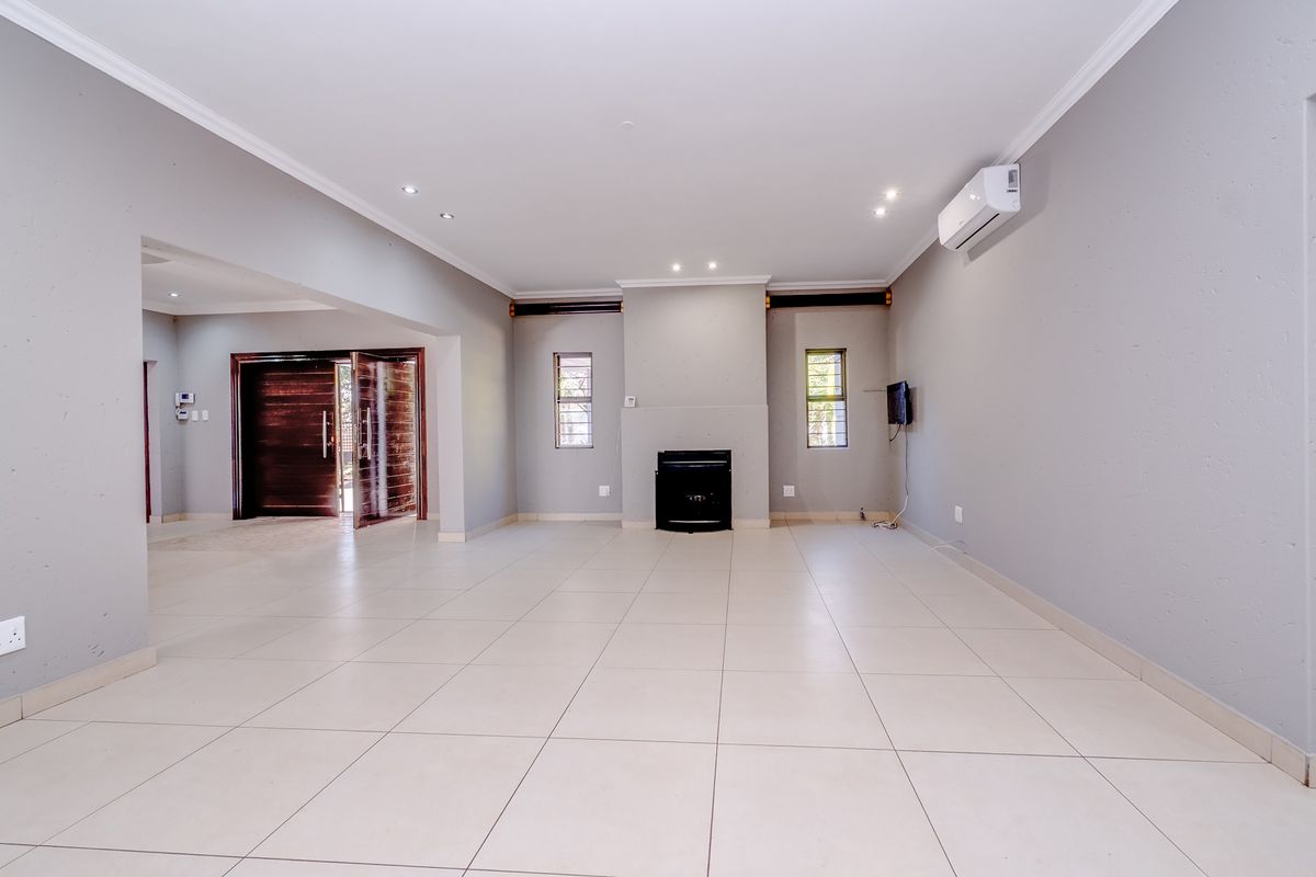Spacious, light-filled living area featuring neutral tiled flooring, a built-in fireplace, and a wall-mounted air conditioning unit, offering a clean and versatile open-plan space.