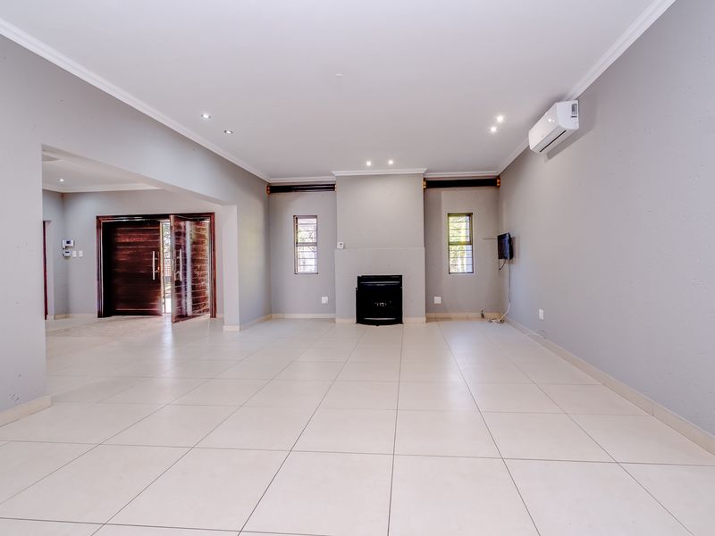 Spacious, light-filled living area featuring neutral tiled flooring, a built-in fireplace, and a wall-mounted air conditioning unit, offering a clean and versatile open-plan space.