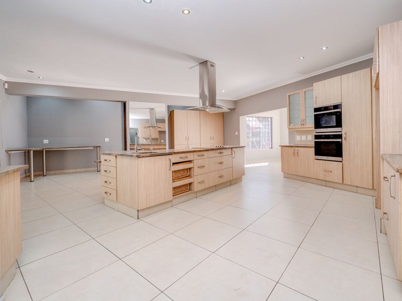Spacious modern kitchen featuring a large central island, light wood cabinetry, built-in appliances, and neutral tiled flooring throughout.