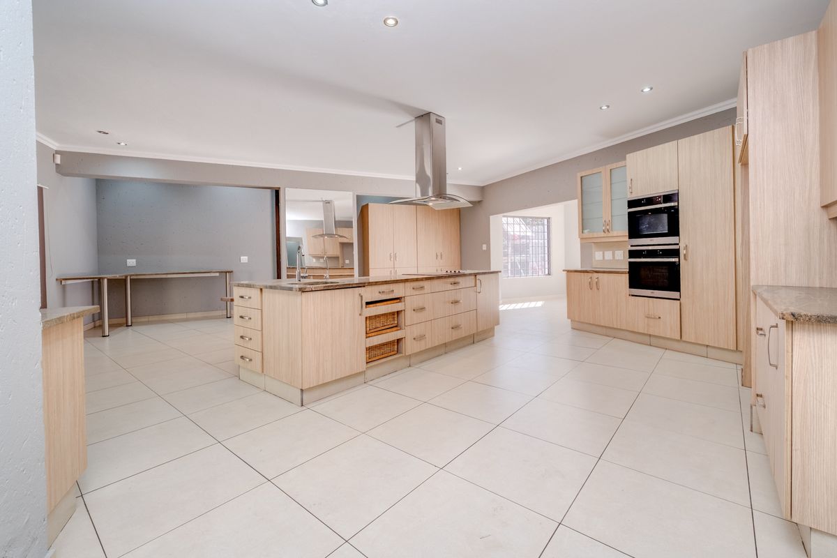 Spacious modern kitchen featuring a large central island, light wood cabinetry, built-in appliances, and neutral tiled flooring throughout.