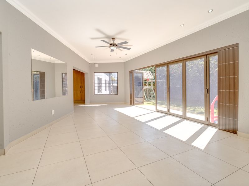Spacious, light-filled living area featuring large sliding glass doors, neutral tiled flooring, recessed lighting, and a ceiling fan.