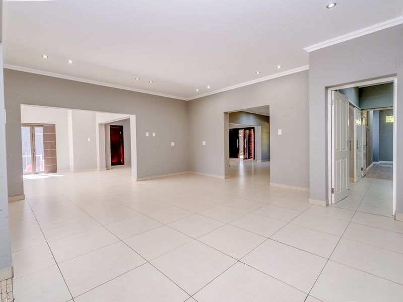 A spacious, open-plan living area featuring neutral grey walls, large format floor tiles, and recessed downlighting, offering a versatile blank canvas for interior design.