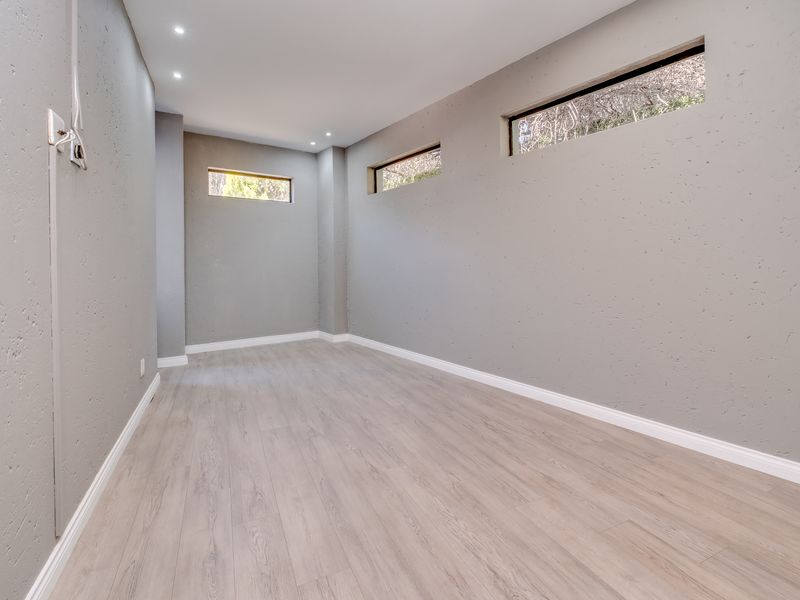 A clean, empty bedroom featuring modern grey textured walls, light wood-look laminate flooring, and high-level clerestory windows providing natural light.