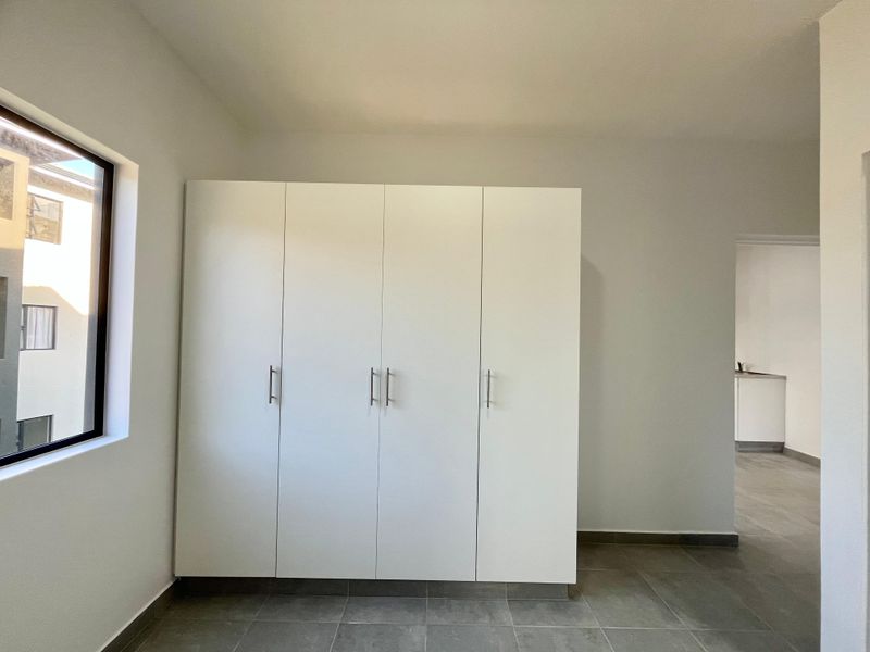 A bright, empty bedroom featuring neutral tiled flooring and a large, modern built-in wardrobe with clean white finishes.