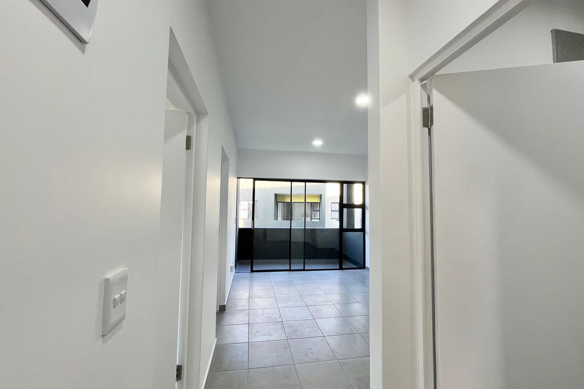 A bright, empty hallway with tiled flooring leading towards a glass sliding door that opens onto a balcony area.
