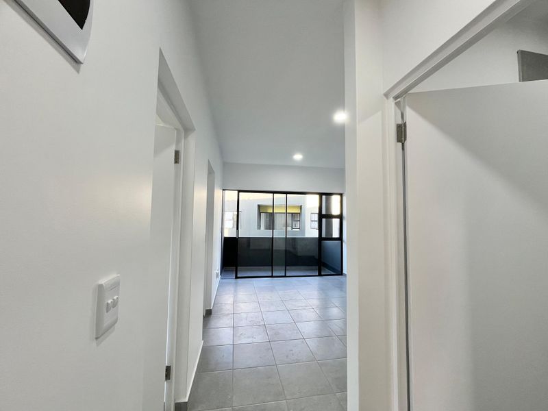 A bright, empty hallway with tiled flooring leading towards a glass sliding door that opens onto a balcony area.