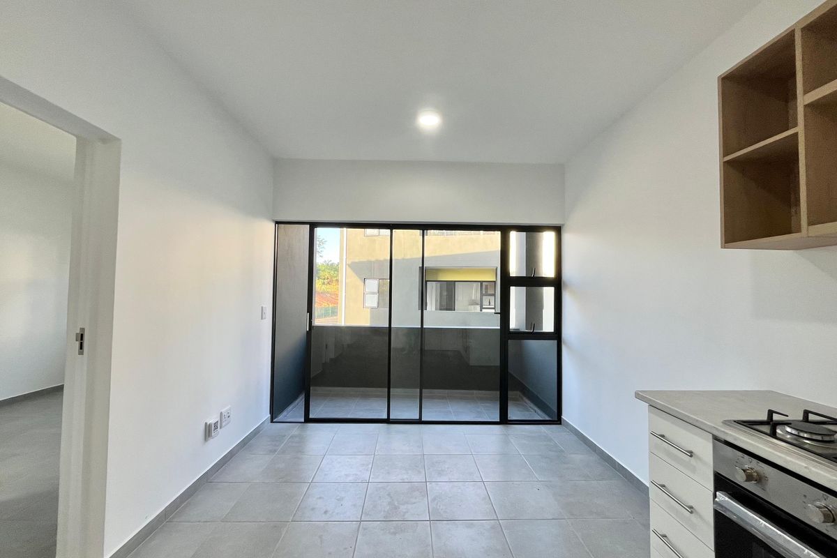 Modern open-plan kitchen and living area featuring tiled floors, built-in oven, gas hob, and large sliding glass doors leading to a balcony.