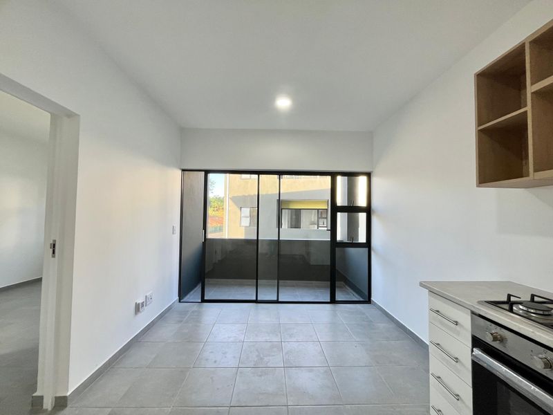 Modern open-plan kitchen and living area featuring tiled floors, built-in oven, gas hob, and large sliding glass doors leading to a balcony.