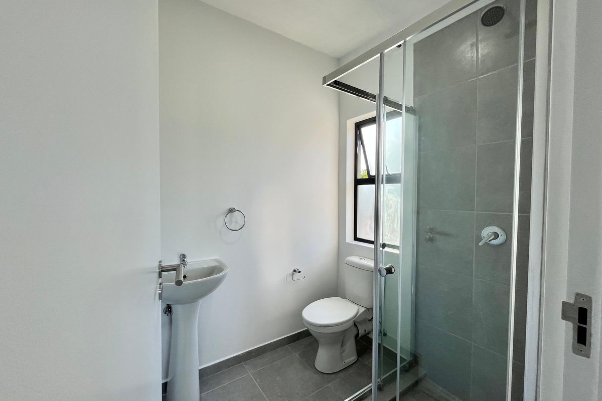A clean, modern bathroom featuring a pedestal basin, toilet, and a glass-enclosed shower with grey tiled finishes.