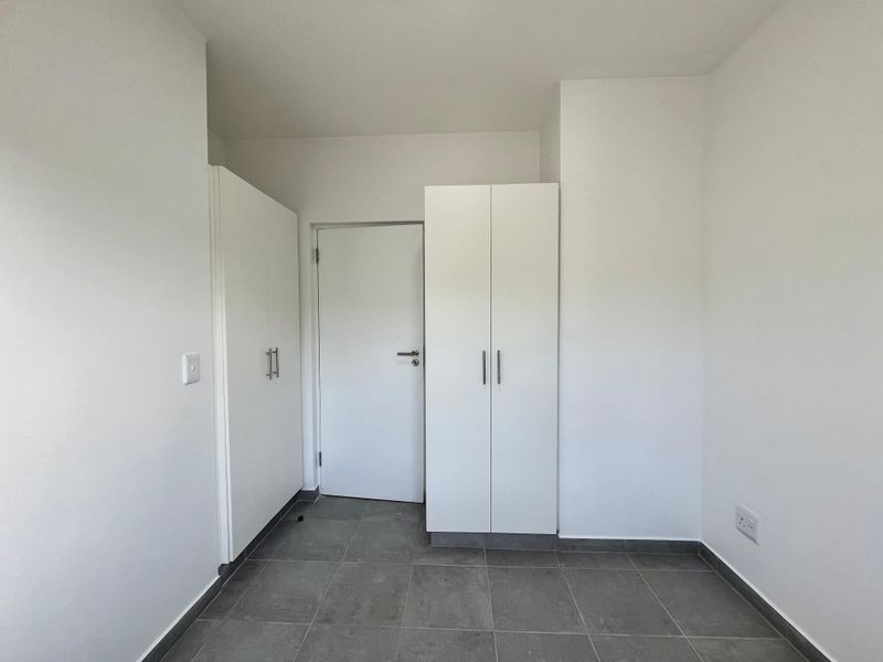 A clean, empty bedroom featuring neutral tiled flooring and white built-in cupboards, offering a blank canvas for personalization.