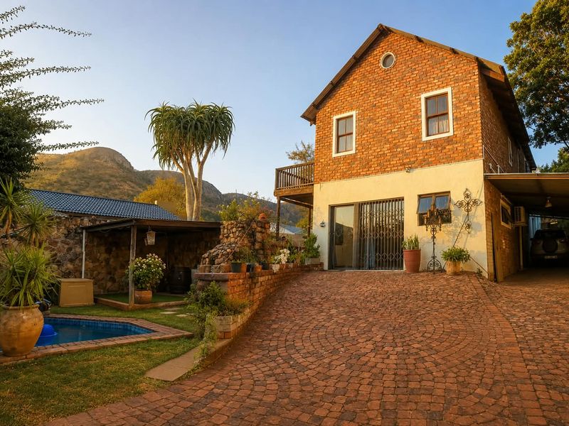 Rear view of a two-story brick house featuring a cobblestone driveway, swimming pool, stone retaining wall, and an attached carport.