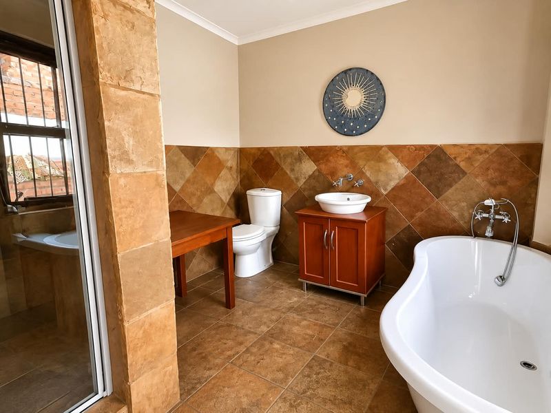 A well-maintained bathroom featuring a freestanding bathtub, a vanity with a vessel sink, and warm-toned wall and floor tiling.