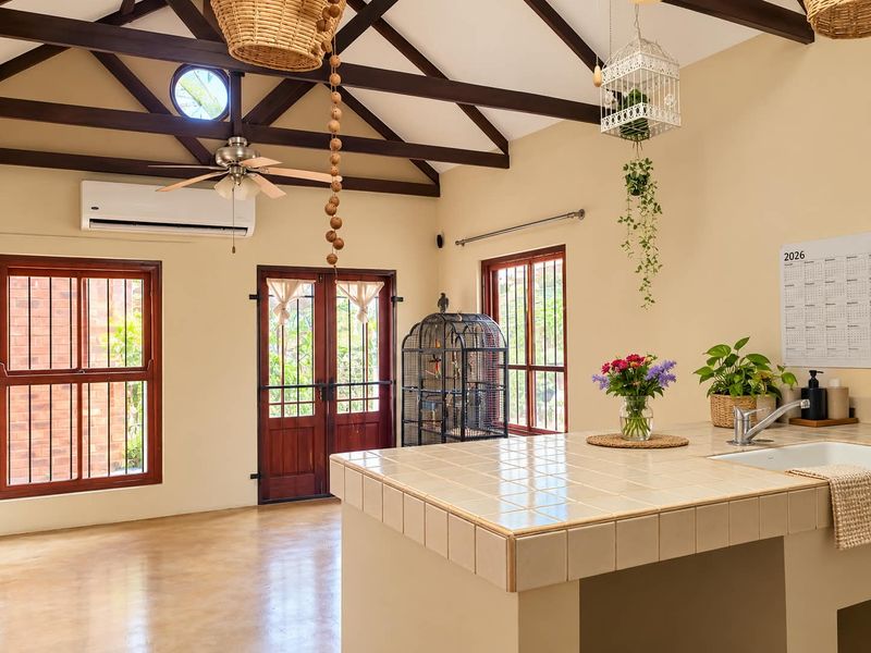 Spacious kitchen area featuring a tiled island, exposed timber ceiling beams, polished concrete floors, and direct access to the exterior through timber framed doors.
