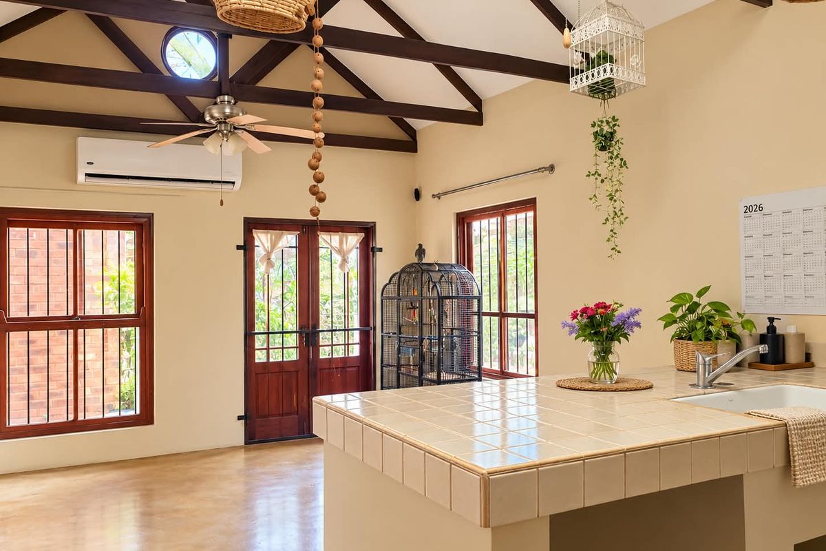 Spacious kitchen area featuring a tiled island, exposed timber ceiling beams, polished concrete floors, and direct access to the exterior through timber framed doors.