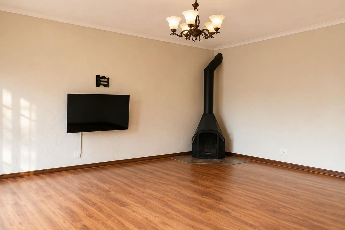 Spacious living room featuring laminate flooring, a corner wood-burning fireplace, and a classic chandelier, offering a clean and neutral canvas for interior design.
