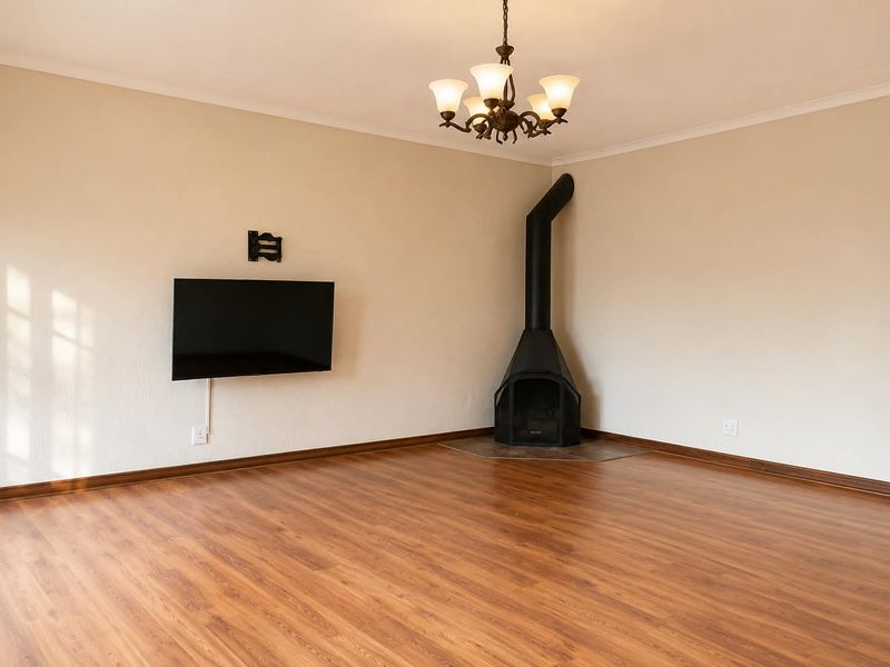 Spacious living room featuring laminate flooring, a corner wood-burning fireplace, and a classic chandelier, offering a clean and neutral canvas for interior design.