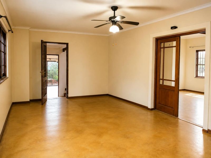 Spacious, empty living area featuring polished concrete floors, a ceiling fan, and classic wooden door frames leading to adjacent rooms.