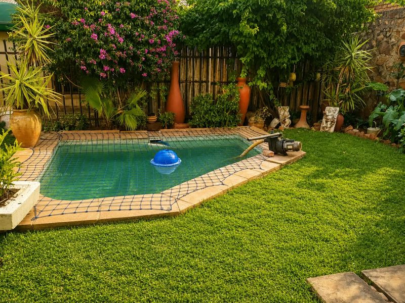 A private backyard garden featuring a swimming pool with a safety net, pump system, and established perimeter landscaping.