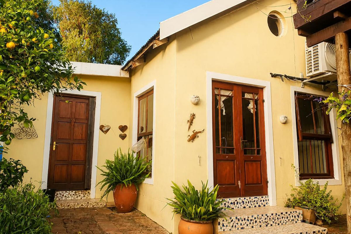 A charming rear exterior view featuring timber doors, tiled entrance steps, and a yellow facade with established garden surroundings.