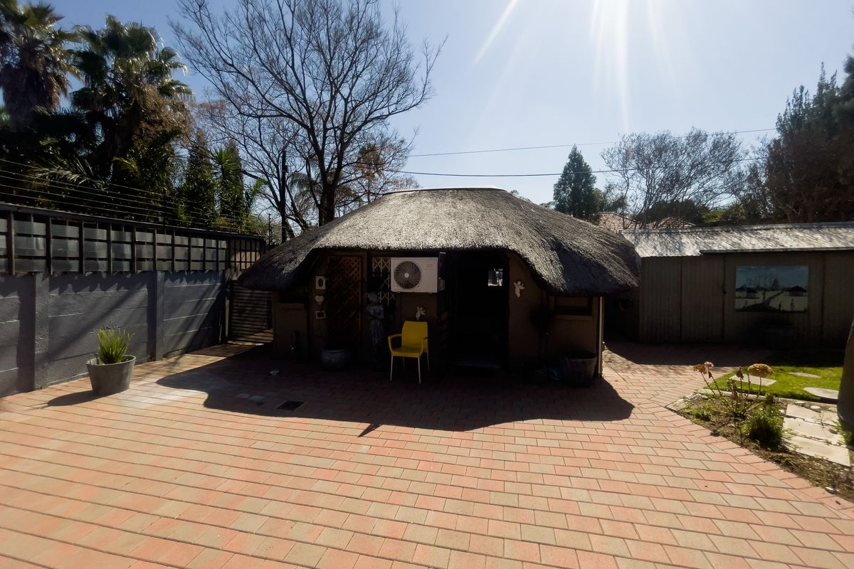 A rear exterior view featuring a thatch-roofed structure with an attached air conditioning unit, set within a paved courtyard area.
