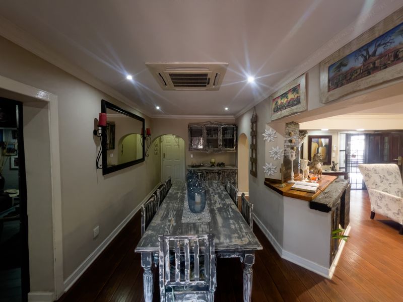 A dining room featuring hardwood flooring, crown molding, and a ceiling-mounted air conditioning unit, with an open-plan layout connecting to adjacent living spaces.