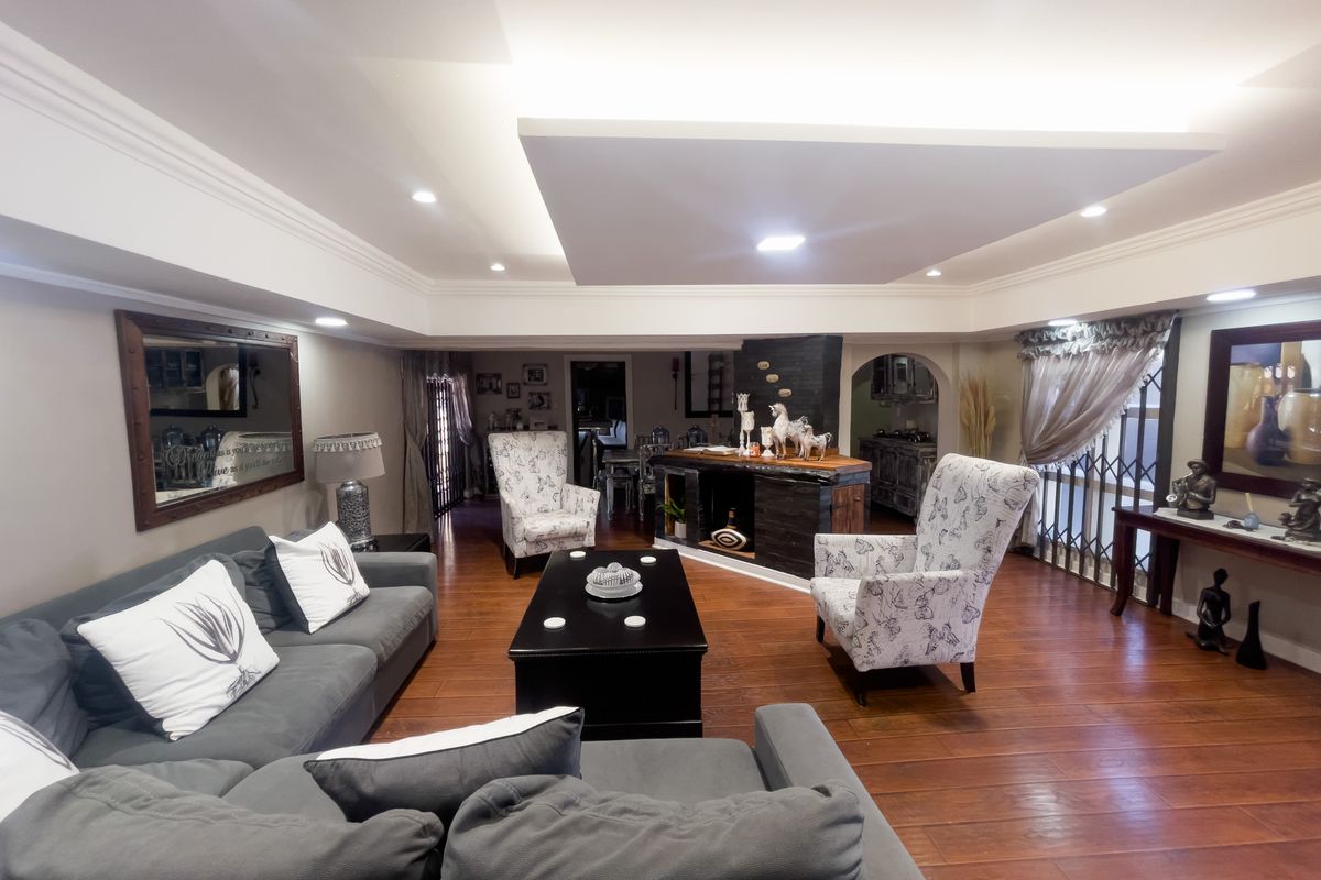 Spacious living room featuring a recessed ceiling with integrated lighting, warm laminate flooring, and a built-in bar area.
