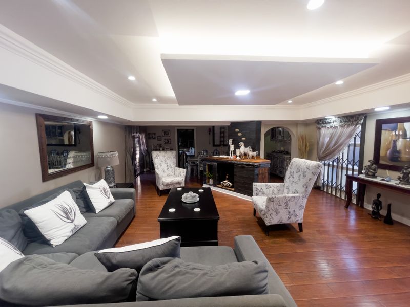 Spacious living room featuring a recessed ceiling with integrated lighting, warm laminate flooring, and a built-in bar area.