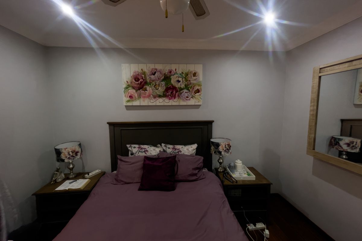 A cozy bedroom featuring timber flooring, recessed downlighting, and a ceiling fan, providing a comfortable and well-maintained sleeping space.