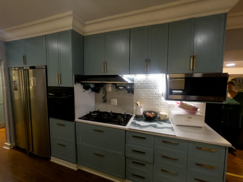 Modern kitchen featuring blue cabinetry, stone countertops, subway tile backsplash, integrated gas hob, extractor fan, and built-in oven and microwave appliances.
