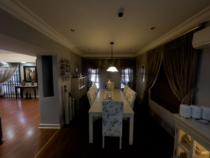 A dining room featuring laminate flooring, recessed lighting, and a wall-mounted air conditioning unit, with an open-plan flow to the adjacent living area.