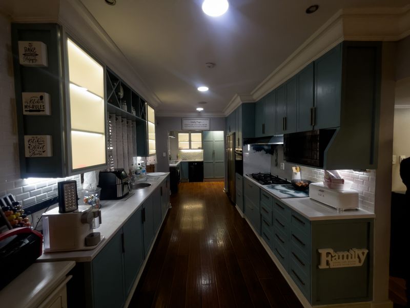A well-appointed galley kitchen featuring dark blue cabinetry, hardwood flooring, integrated lighting, and a subway tile backsplash with modern built-in appliances.
