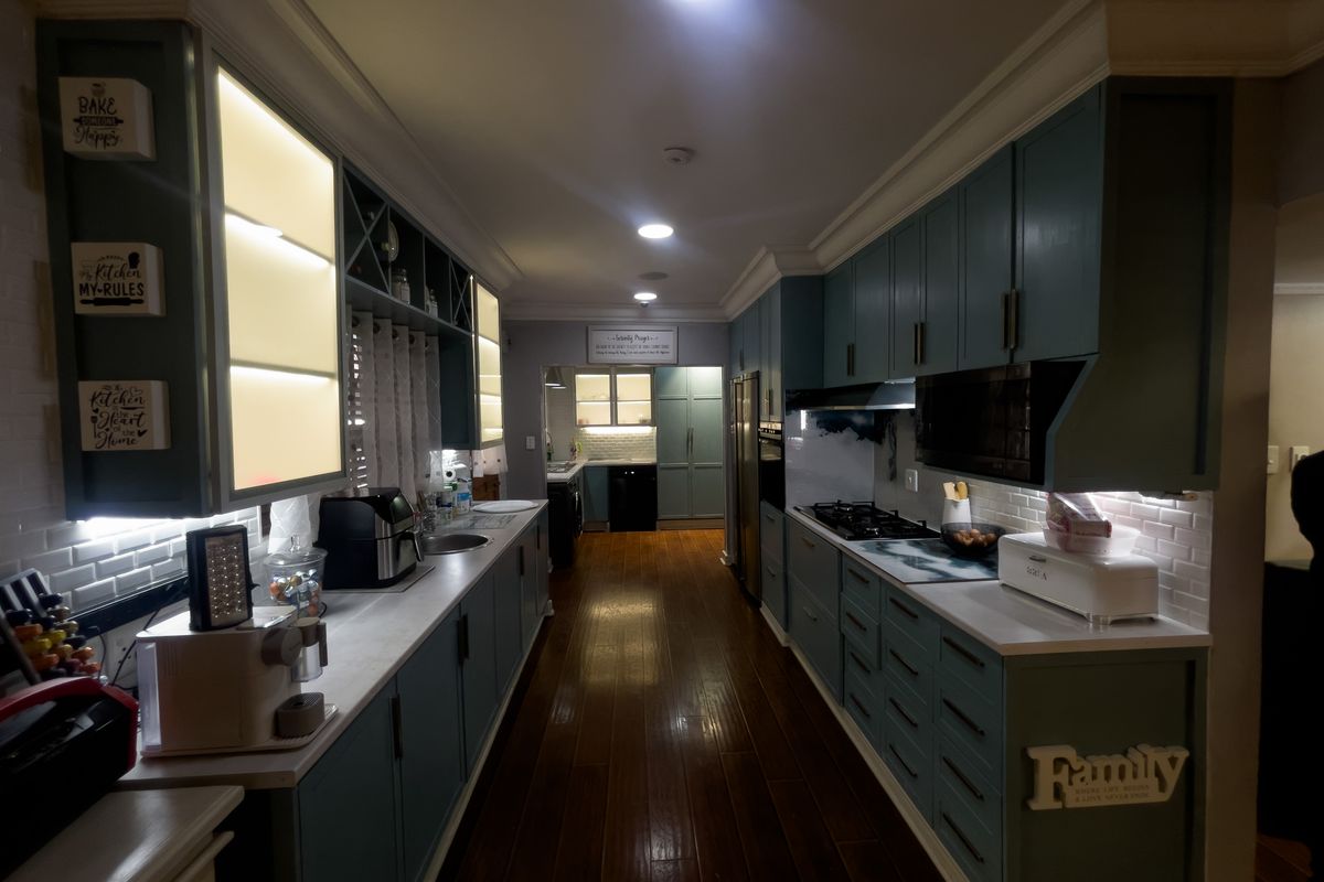 A well-appointed galley kitchen featuring dark blue cabinetry, hardwood flooring, integrated lighting, and a subway tile backsplash with modern built-in appliances.