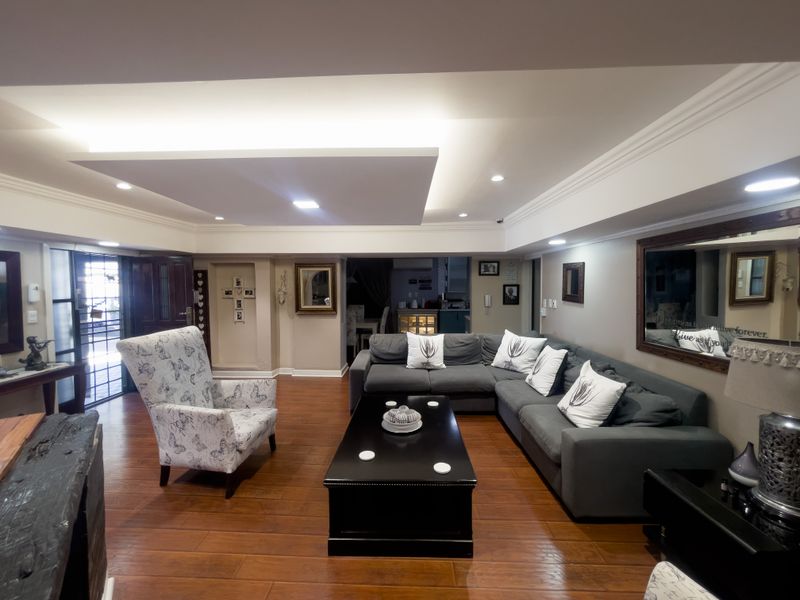 Spacious living room featuring warm hardwood flooring, a modern recessed ceiling with integrated cove lighting, and a secure entrance gate.