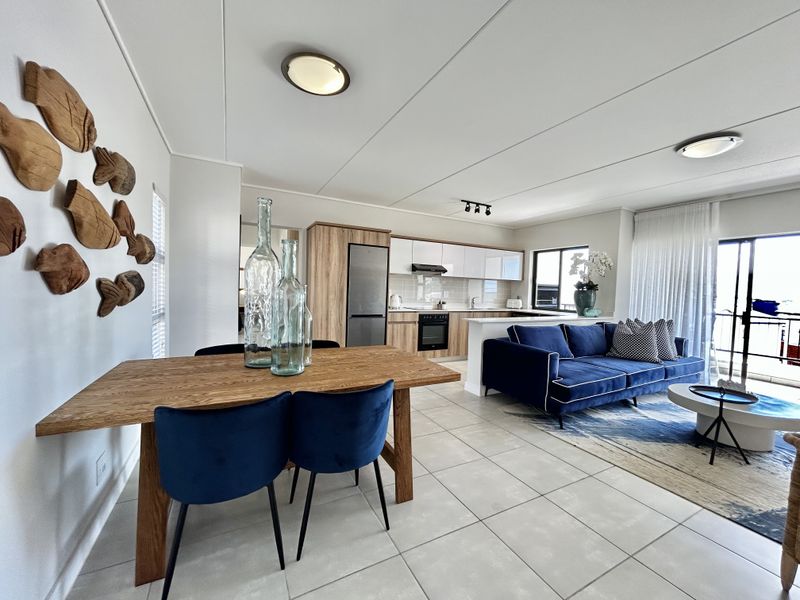 Modern open-plan living area featuring a contemporary kitchen with wood-finish cabinetry, tiled floors, and seamless access to an outdoor balcony.