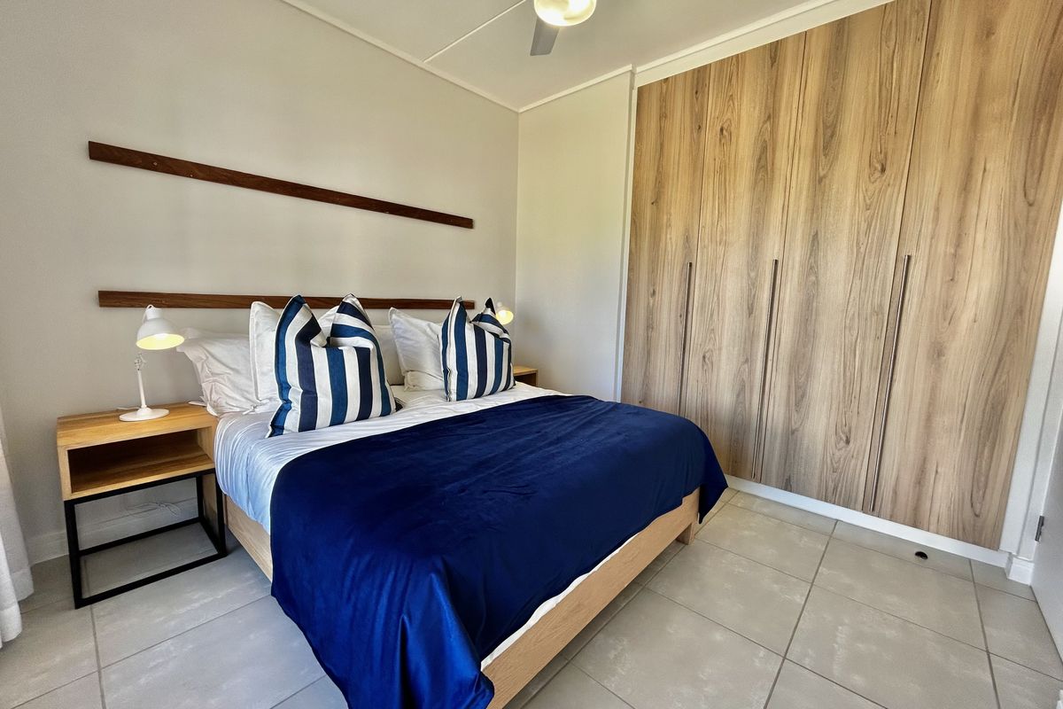 A well-maintained bedroom featuring modern wood-finish built-in cupboards, neutral tiled flooring, and a ceiling fan.
