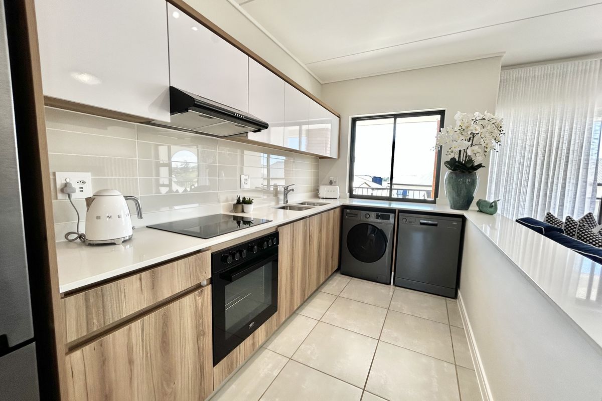 Modern kitchen featuring sleek wood-grain and white cabinetry, quartz countertops, integrated appliances, and a clean subway tile backsplash.