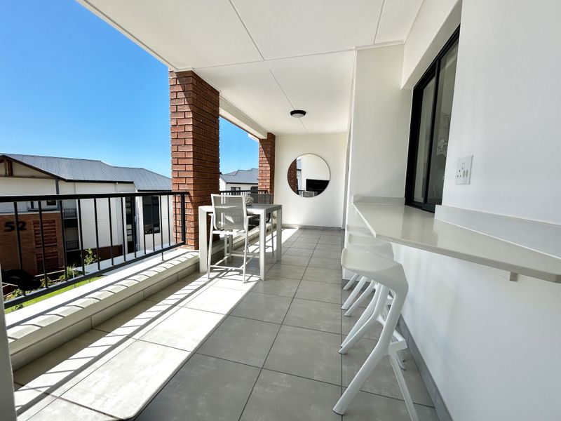 A well-maintained covered balcony featuring tiled flooring, brick structural pillars, a metal balustrade, and a convenient built-in breakfast bar.