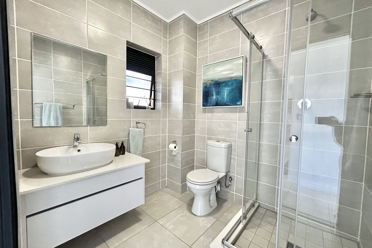 Modern bathroom featuring a floating vanity with vessel sink, glass-enclosed shower, and neutral floor-to-ceiling tiling.