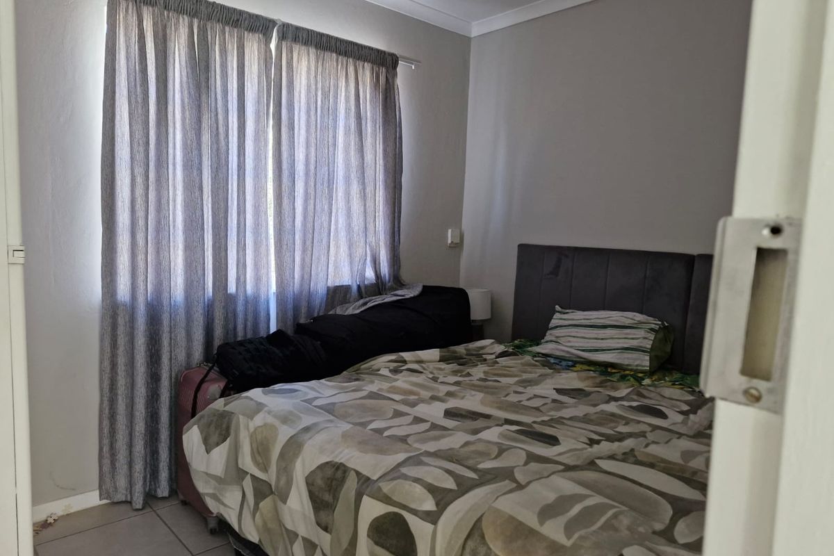 A functional bedroom featuring tiled flooring, neutral wall finishes, and window curtain tracks.