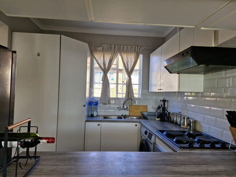 Functional kitchen featuring white cabinetry, subway tile backsplash, laminate countertops, and integrated electric hob with extractor fan.