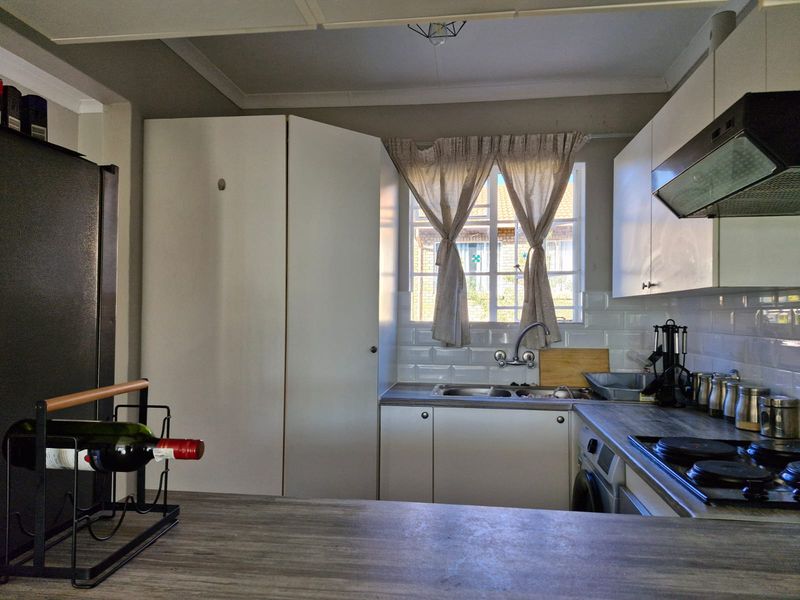 A functional kitchen featuring white cabinetry, subway tile backsplash, integrated hob, extractor fan, and a stainless steel sink under a window.