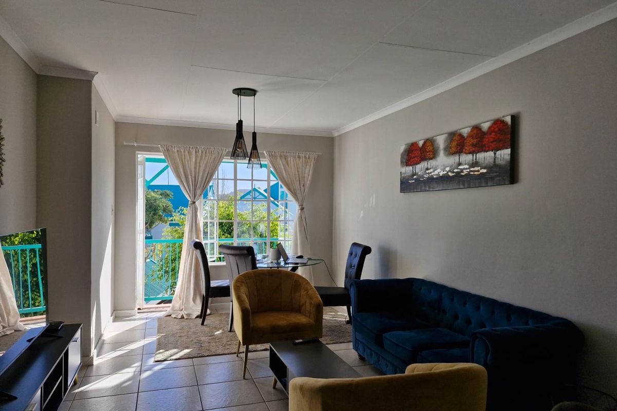 A bright living room featuring tiled flooring, coved ceilings, and a sliding glass door providing access to an outdoor balcony area.