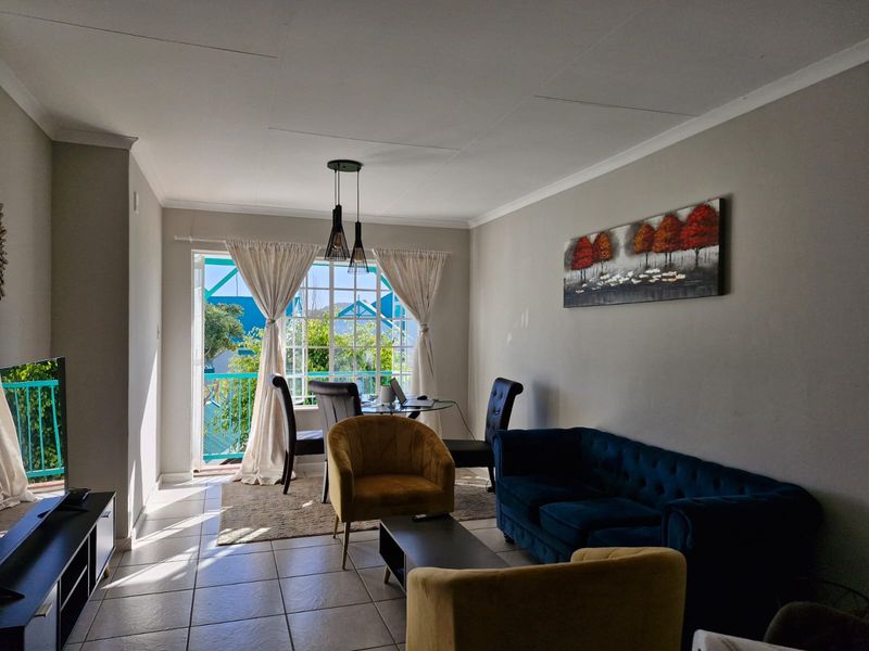 A bright living room featuring tiled flooring, coved ceilings, and a sliding glass door providing access to an outdoor balcony area.