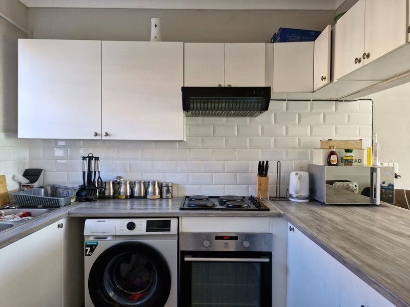 A functional kitchen featuring white cabinetry, a subway tile backsplash, wood-look laminate countertops, and integrated appliances including an oven, hob, and extractor fan.