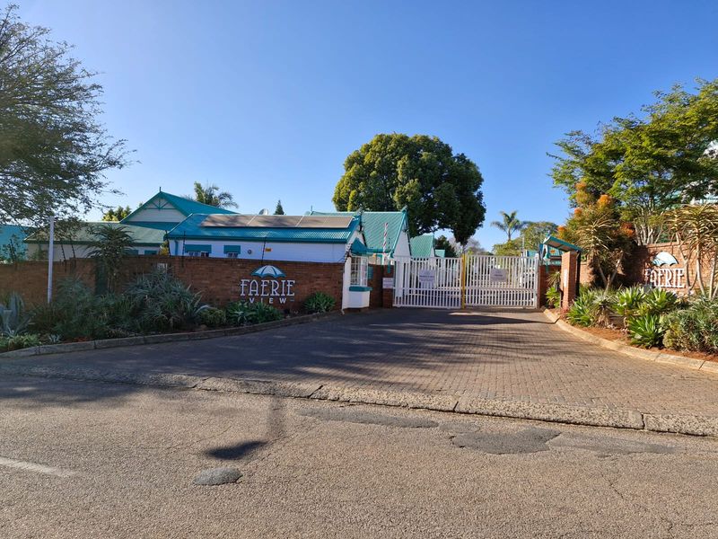 Front entrance view of Faerie View complex featuring a secure gated access point, brick boundary wall, and paved driveway.