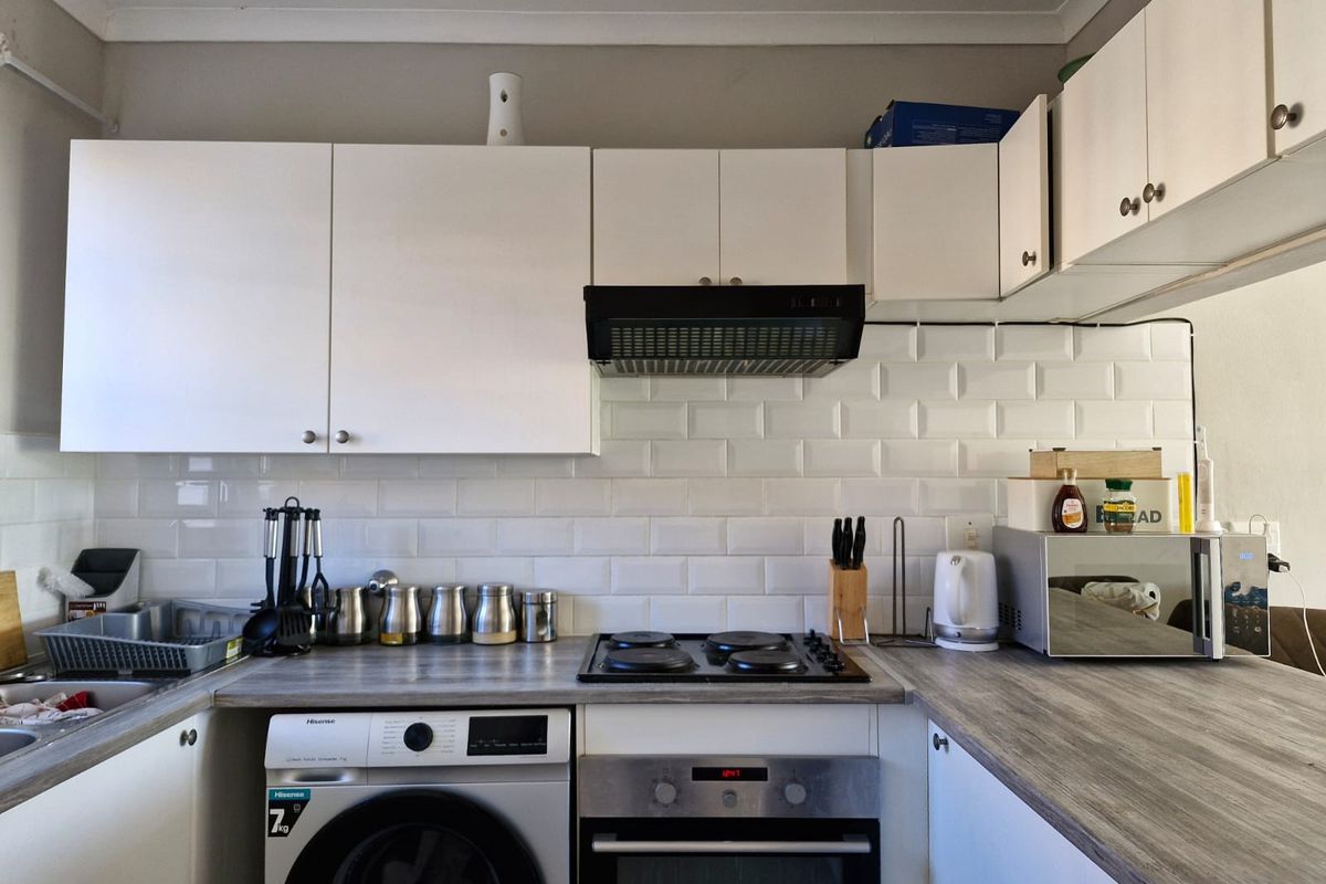 A functional kitchen featuring white cabinetry, a subway tile backsplash, wood-look laminate countertops, and integrated appliances including an oven and hob.